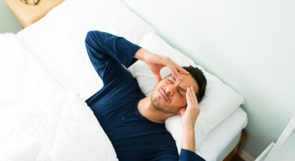 Mężczyzna leżący w łóżku, pocierający skronie przez ból głowy po przebudzeniu - bezdech-senny.info.pl